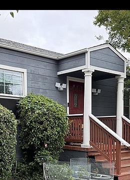 The deep red front door of 310 Oak Ave, framed by white porch columns, the gable peak overhead, and the blue clapboard siding behind it